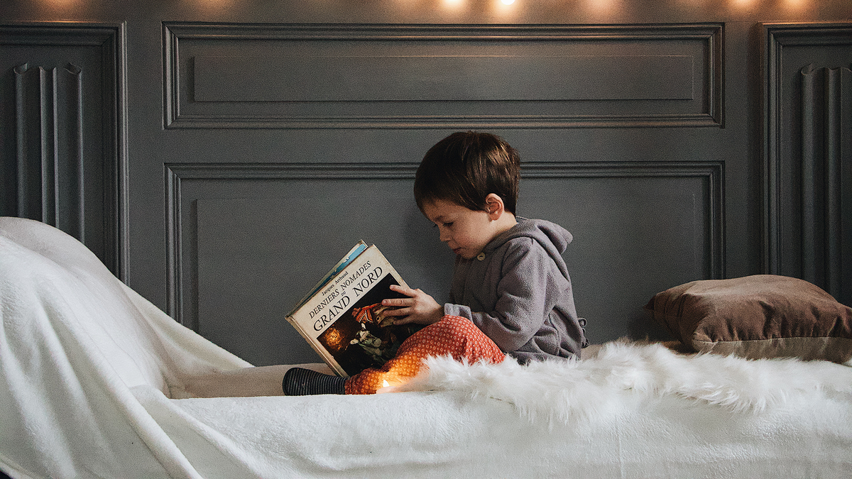 Young boy sits on bed with holiday lights reading a classic Christmas story.