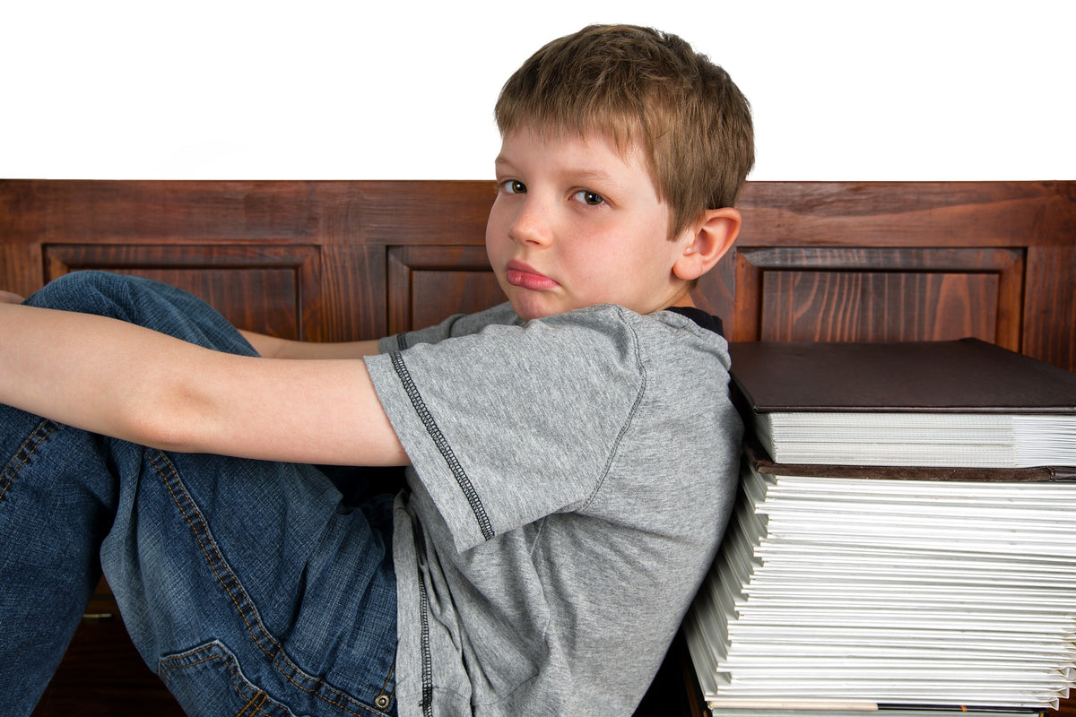 A 6-year-old boy leans on a stack of books appearing deflated. Homework isn't always easy, but with a few tips and tricks you and your child can get through it with relative ease after some practice.