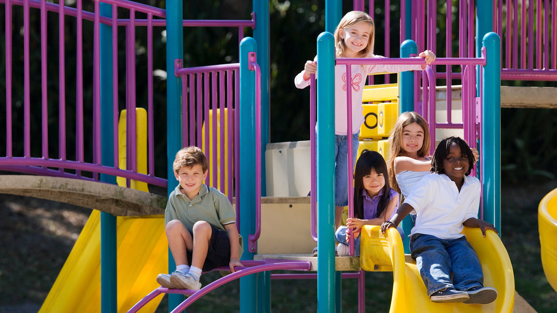 A group of children sit on a slide at a playground, smiling at the camera