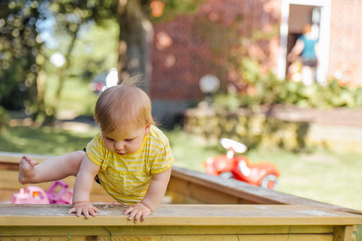 1-Year-Old girl lifts a foot up to crawl out of a sand box. A 1-year-old's motor skills are rapidly developing and can be strengthened with simple activities.