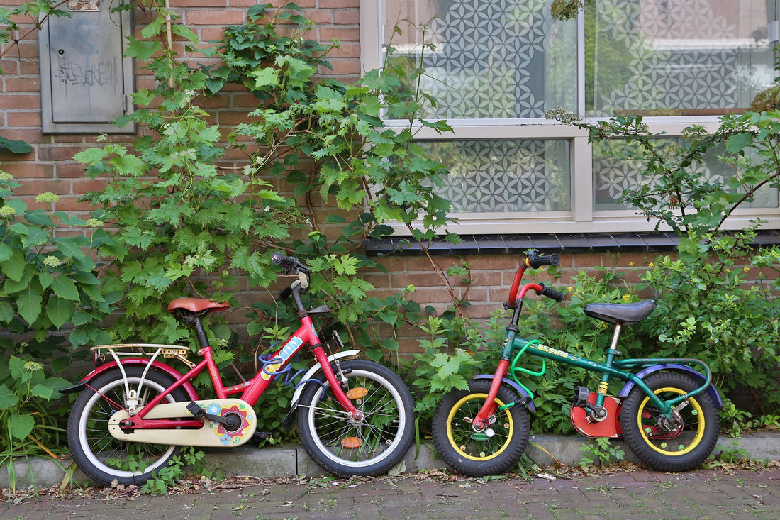 Two colorful children's bikes are parked facing each other outside of a brick building with greenery. Going on a family bike ride is one free activity you can try out with your toddler this weekend for some family fun.