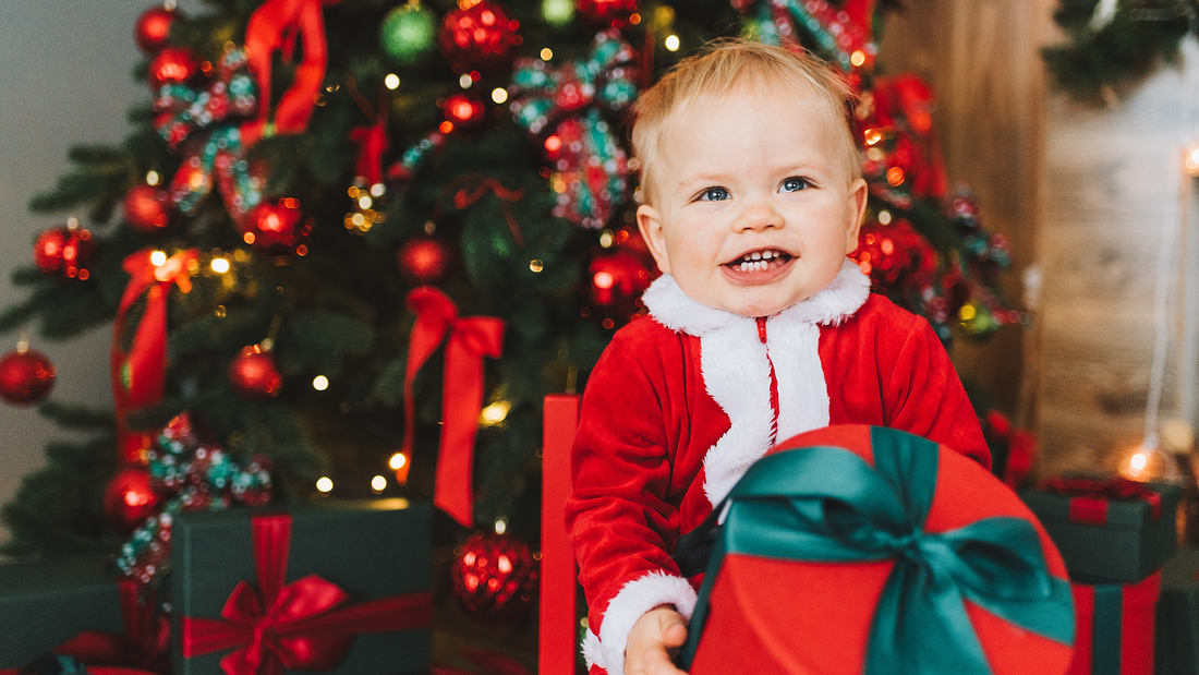 Excited baby boy holds present in front of Christmas tree.