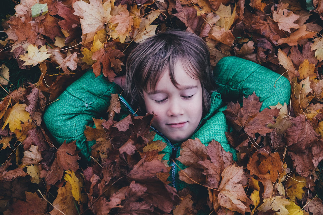 6-year-old boy lays in a pile of leaves with a relaxed expression on his face. There are several methods to help your child focus that will lead to task completion in a calm and collected manner.