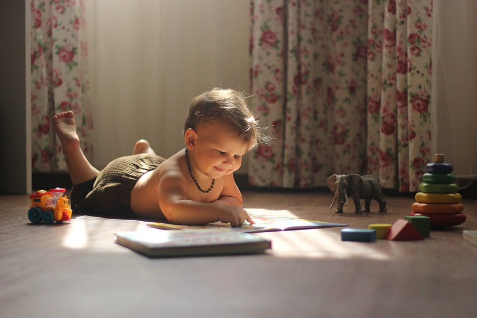 1-year-old baby lays on his stomach and plays with wooden toys and books. There are many screen-free ways to engage your child when you are busy.