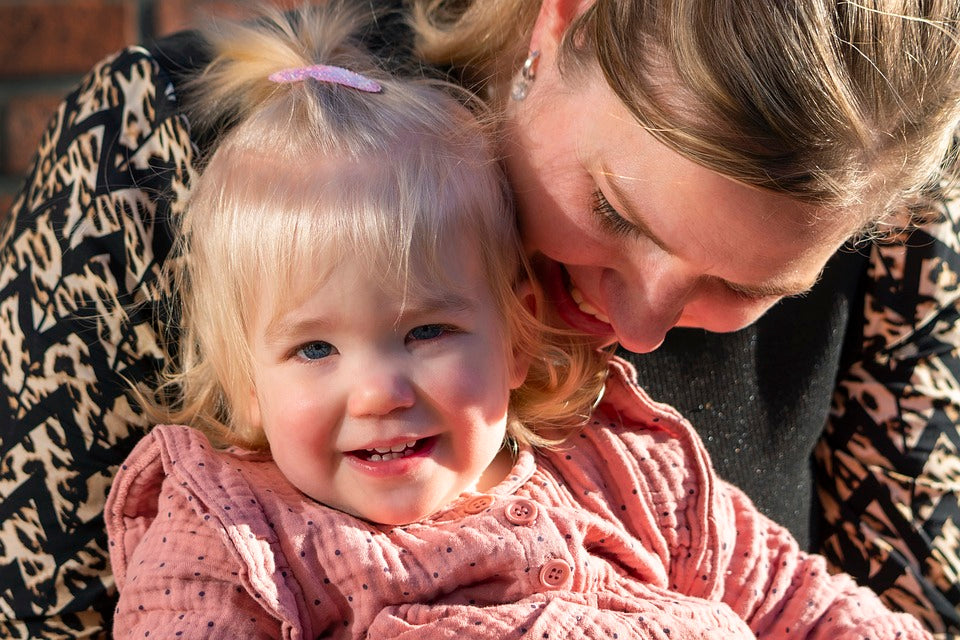 1-year-old girl talks with her mother while sitting on her lap. Parents should start pulling back on baby talk between 18-24 months, as their child's language starts becoming more complex.