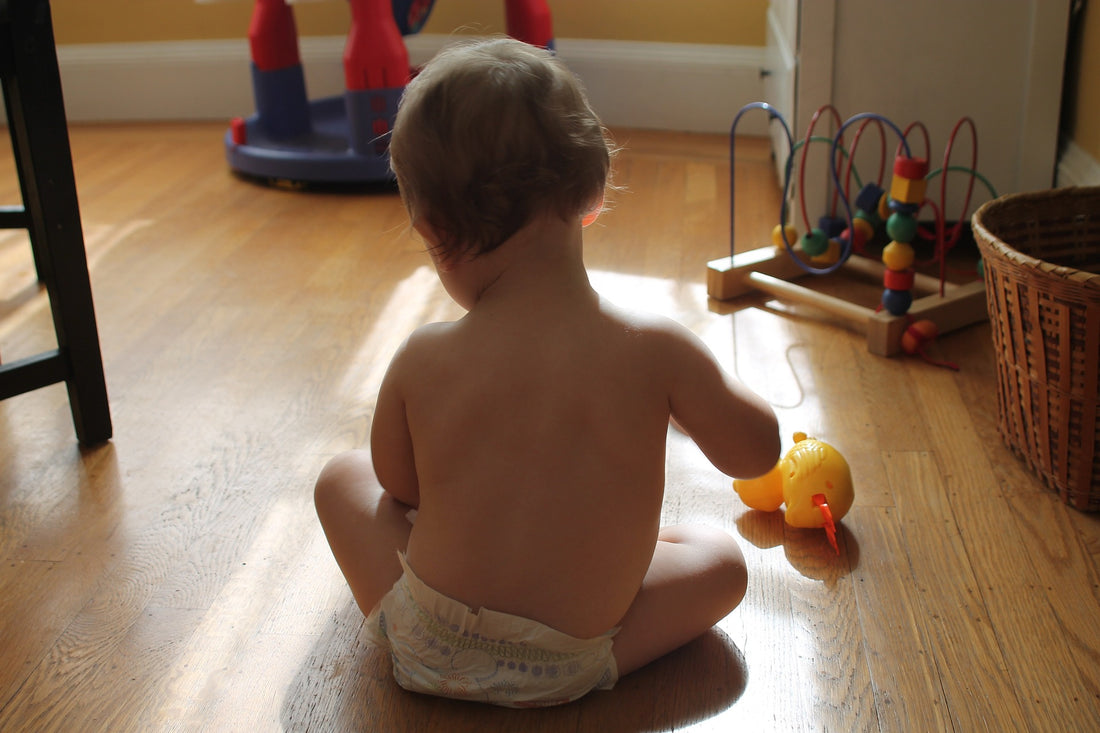 One-year-old child in a diaper sits on the floor of his home surrounded with child-safe toys. Baby proofing your home when your little one gets mobile is essential to their safety.