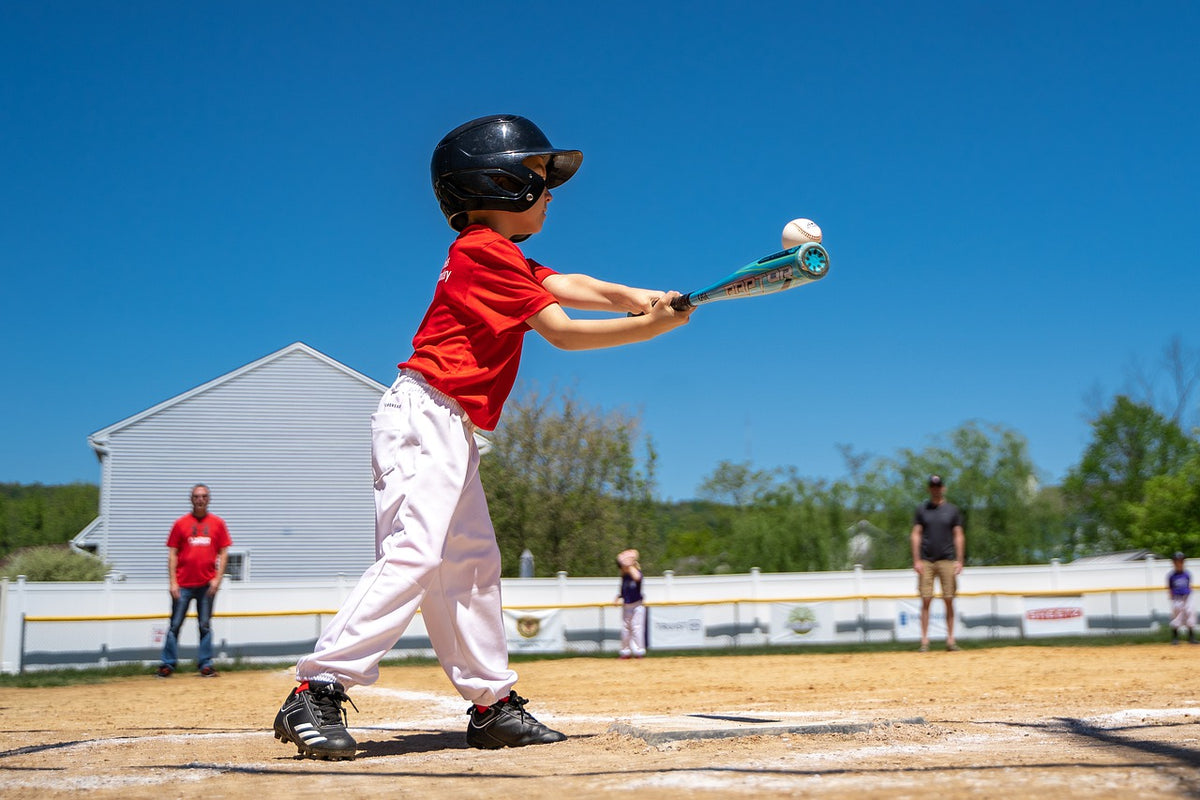 6-year-old boy in baseball uniform swings his bat and hits the ball. Enrolling your child into organized sports is one way to keep them regularly active at this age.