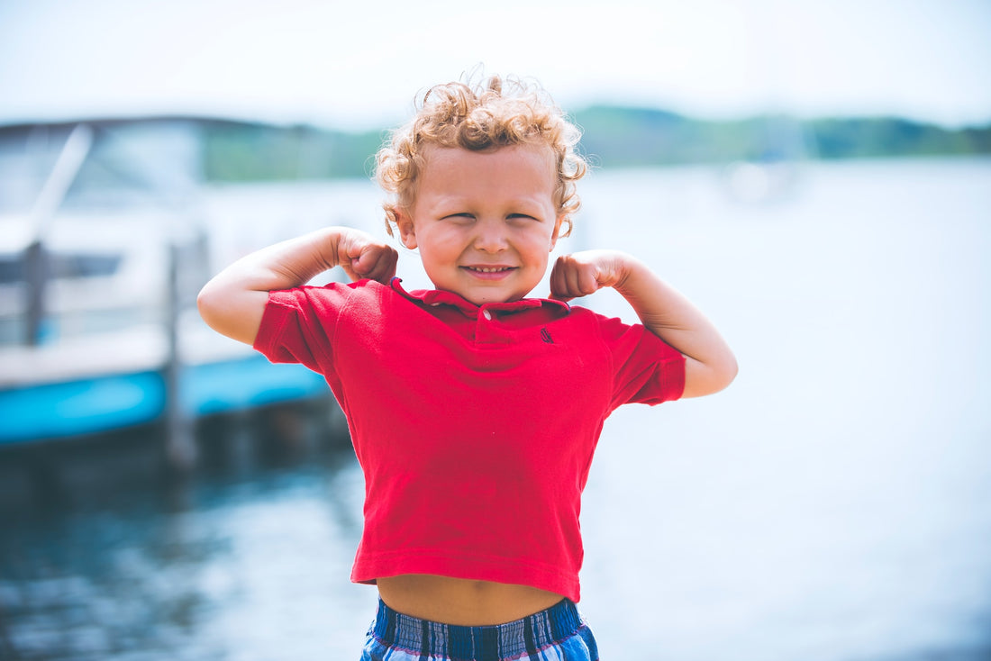 Two-year-old boy in red shirt flexes his muscles with a smile. Your child will reach a multitude of new milestones in his or her 2nd year of life.