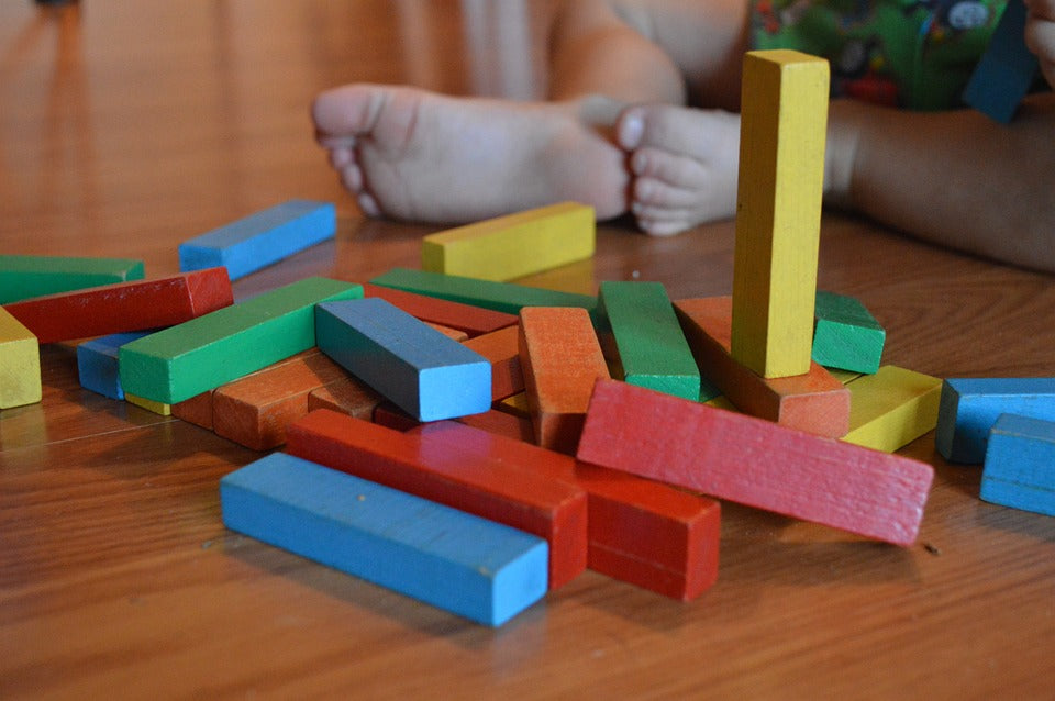 Wooden blocks lay scattered at a child's feet. Stacking blocks is a simple activity that encourages problem solving skills in young children.