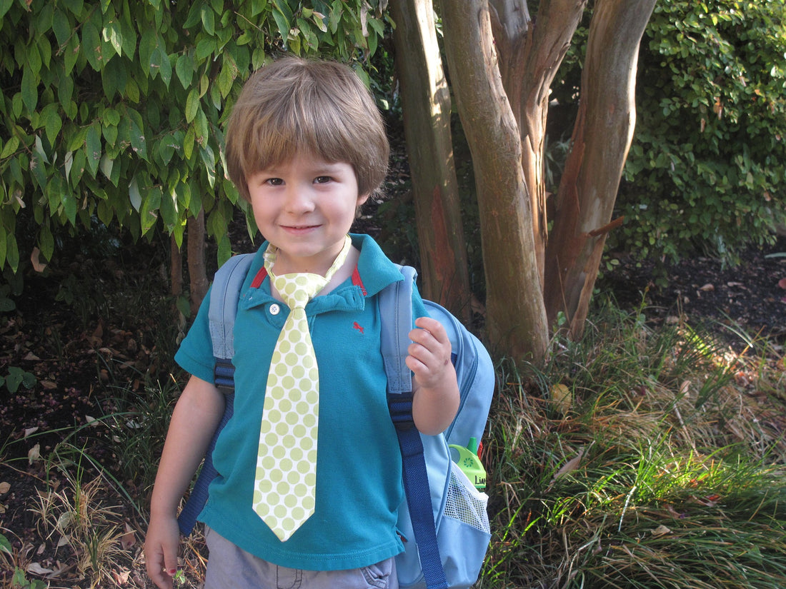 4-year-old boy wearing a tie stands outside with his bookbag on. As your child starts traveling to and from school, it's important for their safety that they memorize their phone number and address in case of emergency.