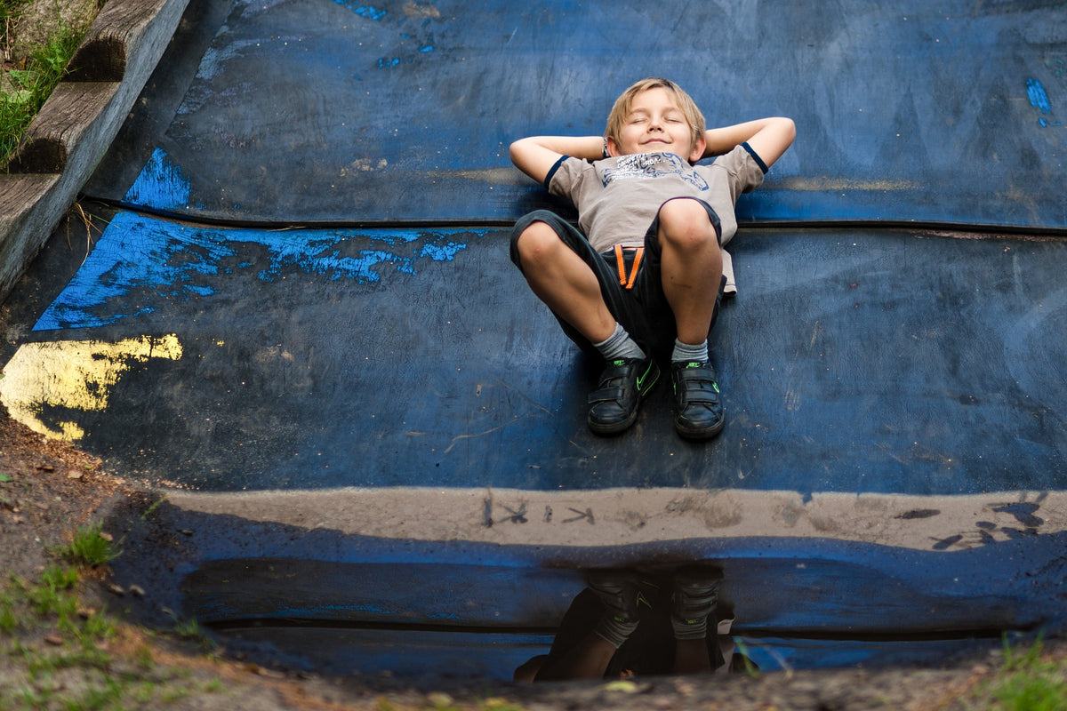5-Year-Old boy lies on the ground with his eyes closed, a smile on his face, and his hands behind his head. Teaching your child to keep a "calm body" is a great way to set them of for success in the area of self-regulation.