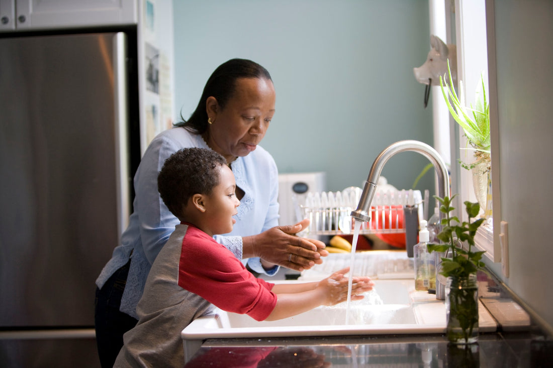 Grandmother and 3-year-old grandson stand together at the sink washing up. 3-year-old are eager to be helpers and giving them chores to do will help them feel a sense of independence and accomplishment.