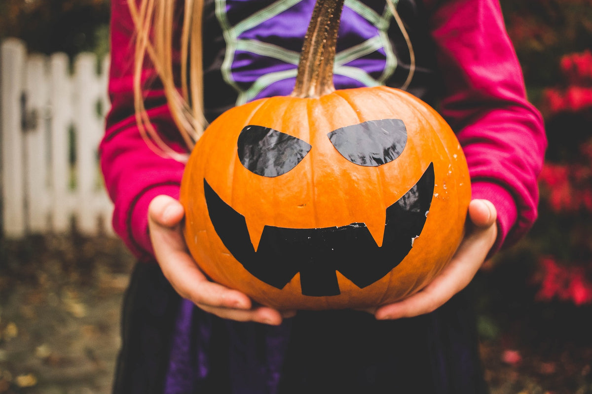 Child in costume holds a jack-o-lantern