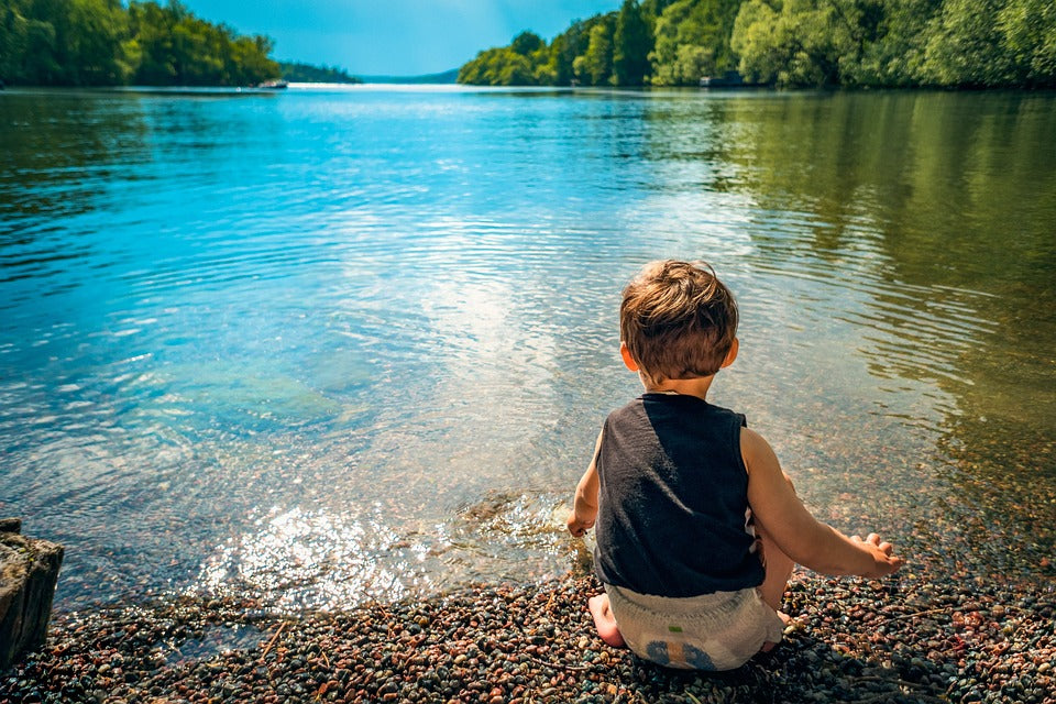 1-Year-Old boy squats down and plays with water at a sunny lake. At this age, your child will be engaging in functional play, which is an important part of their development.
