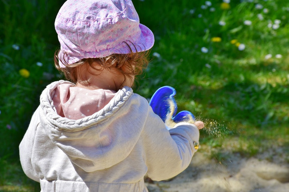 One-year-old girl experiments with cause and effect by pouring sand out of a plastic container.