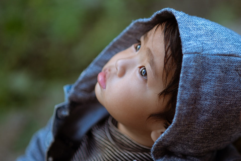Two-year-old boy with a hooded jacket on stares up at the sky. At this age, your toddler is making rapid development in their understanding of language, emotion, social interactions, time, cause and effect, and much more!