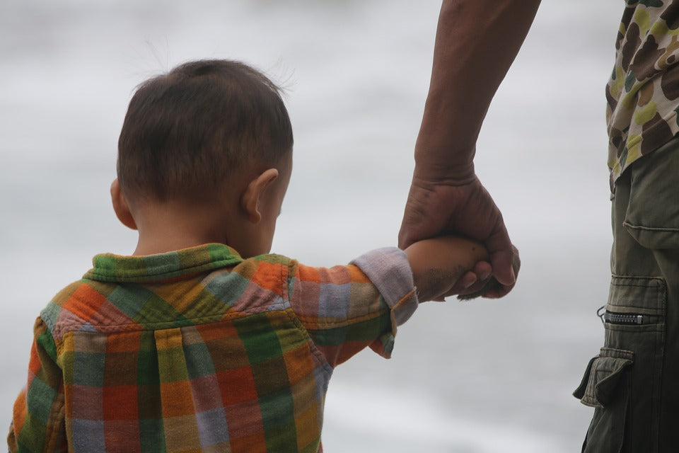 A 1-year-old boy walks hand in hand with his father. Most children will begin walking at between 10-18 months of age. Providing opportunities for movement is important for encouraging their motor skill development.