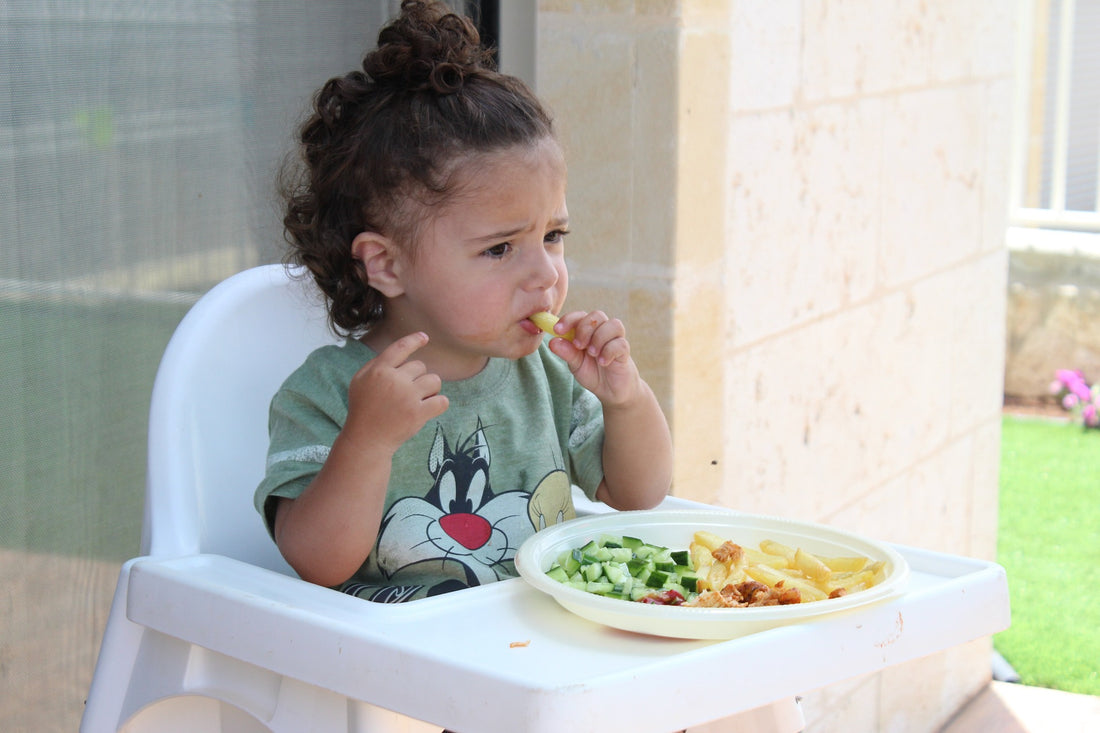 Little girl sits in her highchair, tentatively trying out some new vegetables. Tackling picky eating in toddlers is no small feat, but can be done with modeling, consistency, and some fun choices for healthy eating!