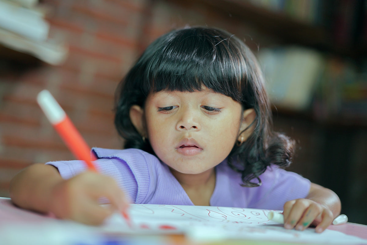  A 3-year-old girl writes her name on a piece of paper using a marker. Writing their name is a great way for a child this age to begin learning their letter formations.