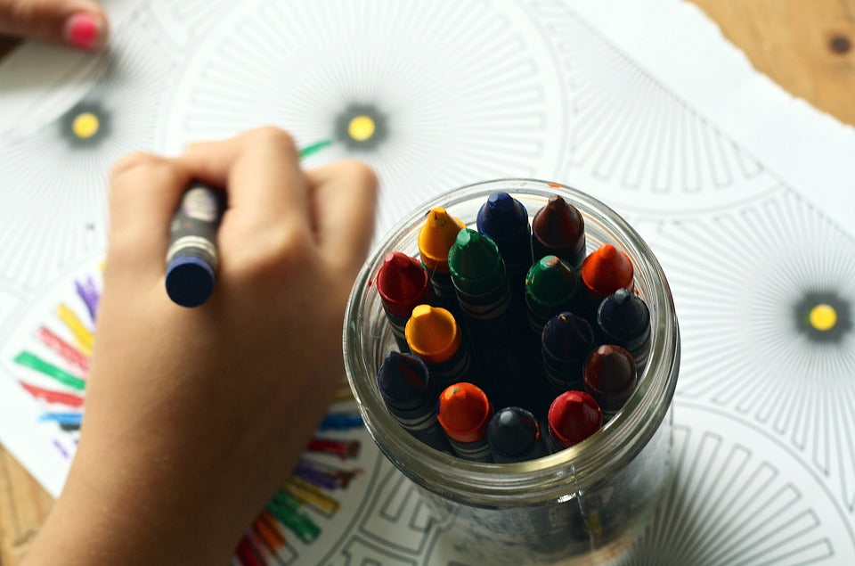 A kindergartener's hand holds a crayon while coloring a picture at a desk. As your child starts school, it's important to set up a consistent after-school routine that reinforces the concepts that they're learning in the classroom.
