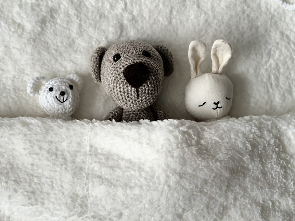 Three child's stuffed animals lie side by side, neatly tucked in with a blanket. Creating a serene, organized environment for your toddler is helpful for fostering independence.