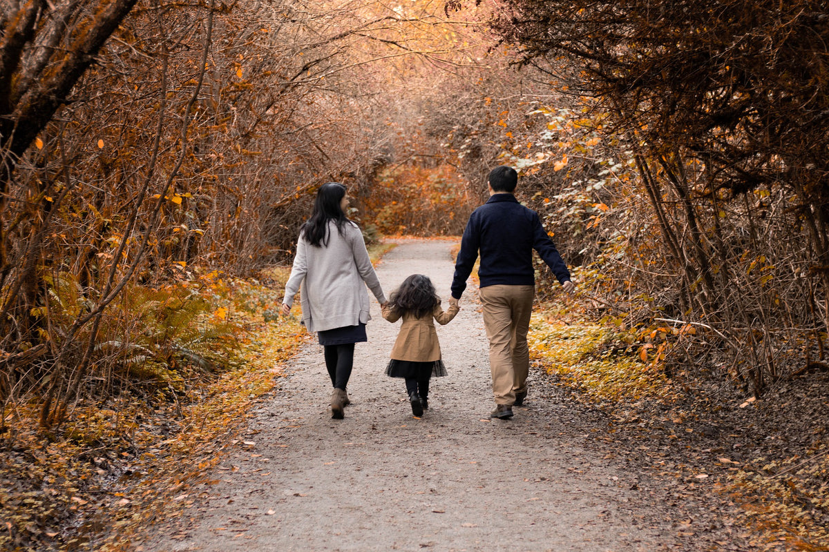 Family walking down a nature path surrounded by falling leaves