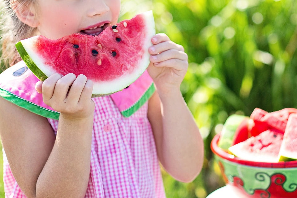 3-year-old girl bites into a large slice of watermelon. Creating healthy eating habits in your child early will set them up with a lifetime of good health.