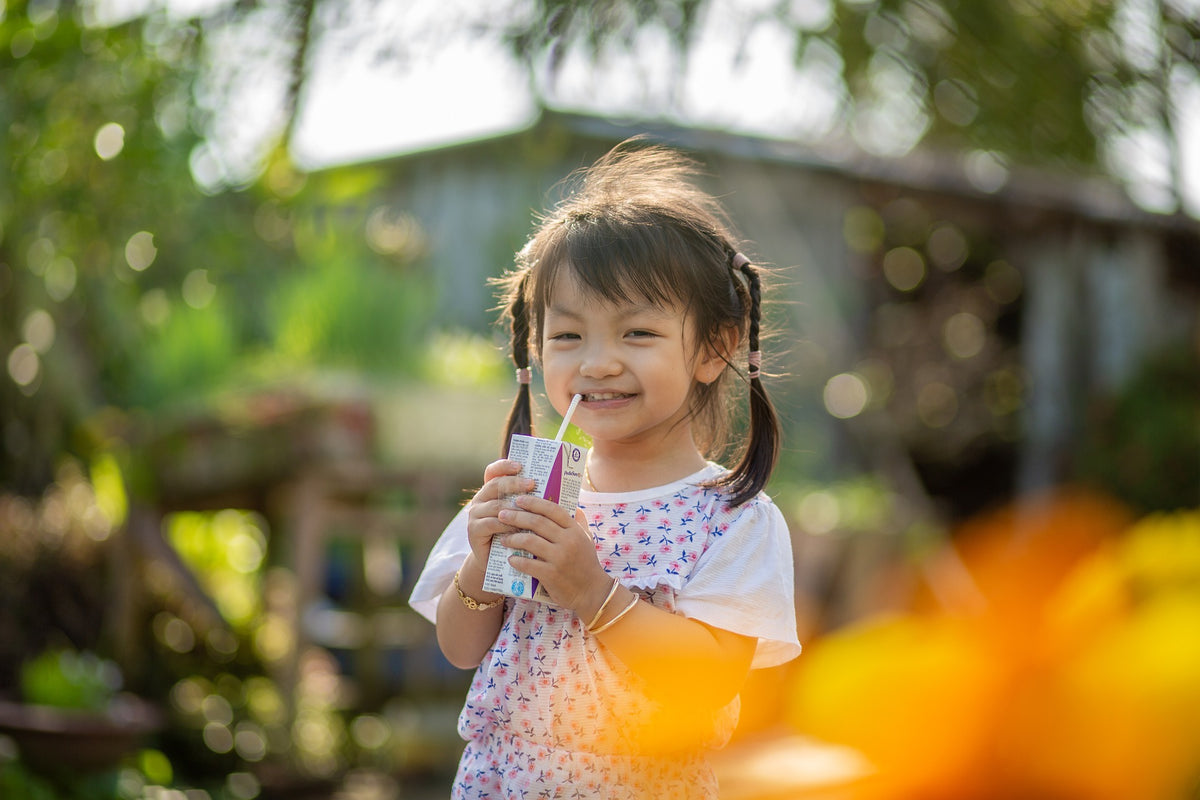 3-year-old girls smiles and sips on a juice box. Teaching your toddler age-appropriate skills that lead to independence will make your little one feel capable!
