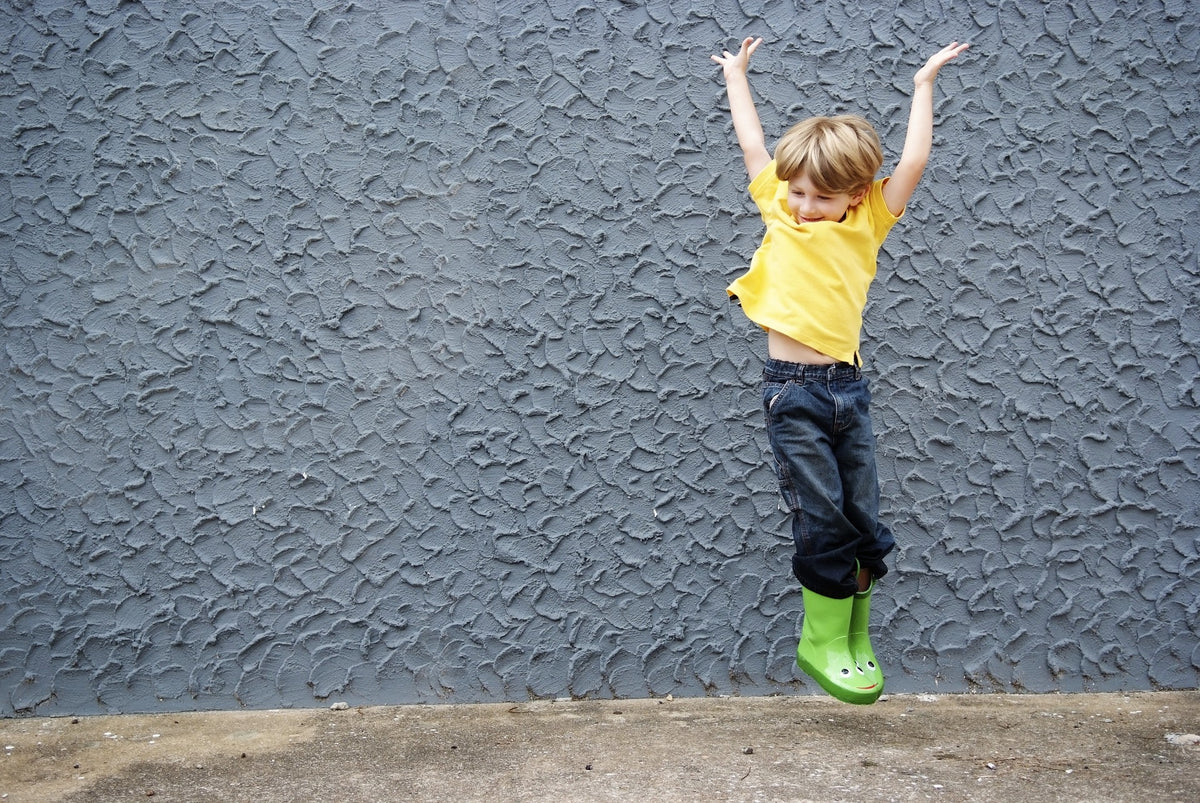 Happy 4-year-old boy in rainboots jumps for joy. Your child will reach another set of gross and fine motor skills milestones this year!