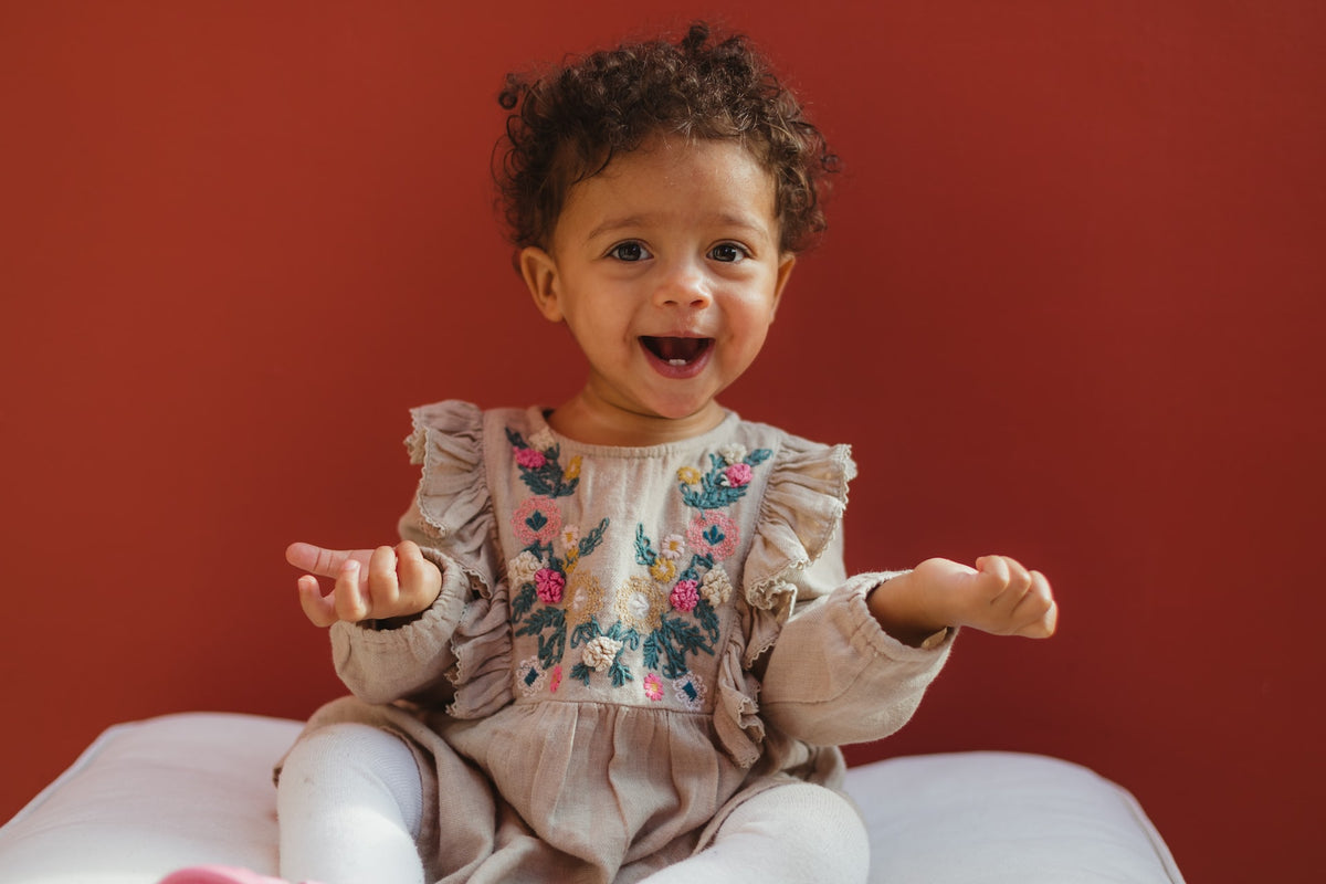 1-year-old girl wears a happy but quizzical expression in front of a red background.