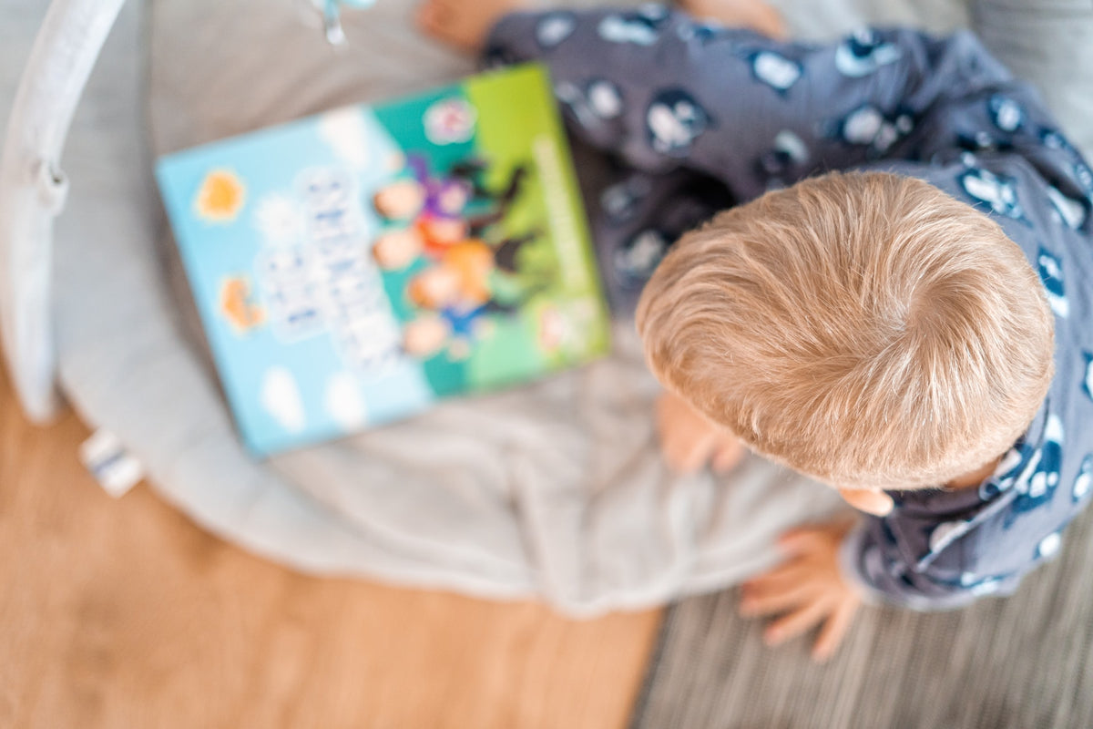 3-year-old boy sits with a book in his lap. Many children can begin recognizing letters at around the age of 3 with regular exposure to books and words.