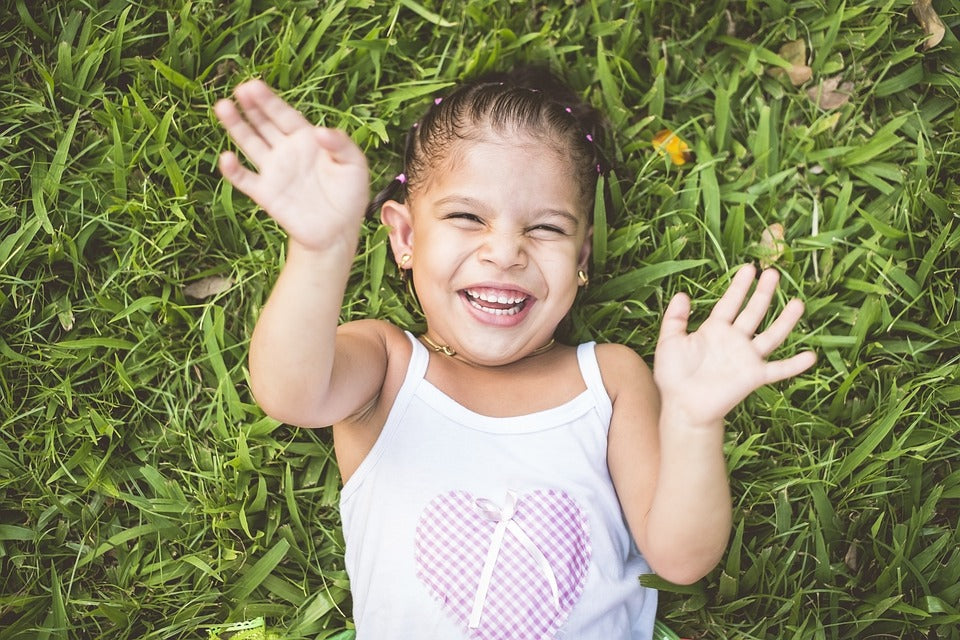 4-year-old girl lies on the grass with a huge smile. There are plenty of fun ways to play with rhyming words that will strengthen your child's literacy skills as they start to read.