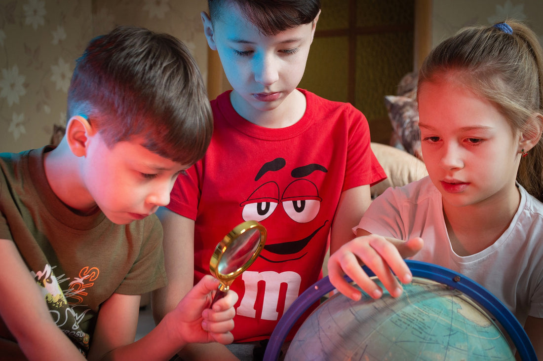A group of three 5-year-olds surround a globe to examine it with a magnifying glass. Teaching your child a growth mindset in important for them to have success in many areas, including academically.