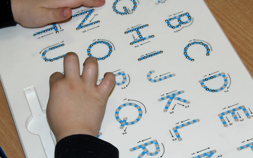 A pair of child's hands trace alphabet letters. Tracing alphabet letters while saying the letter's name and sound is a practice that will help your child solidify this skill if done daily.