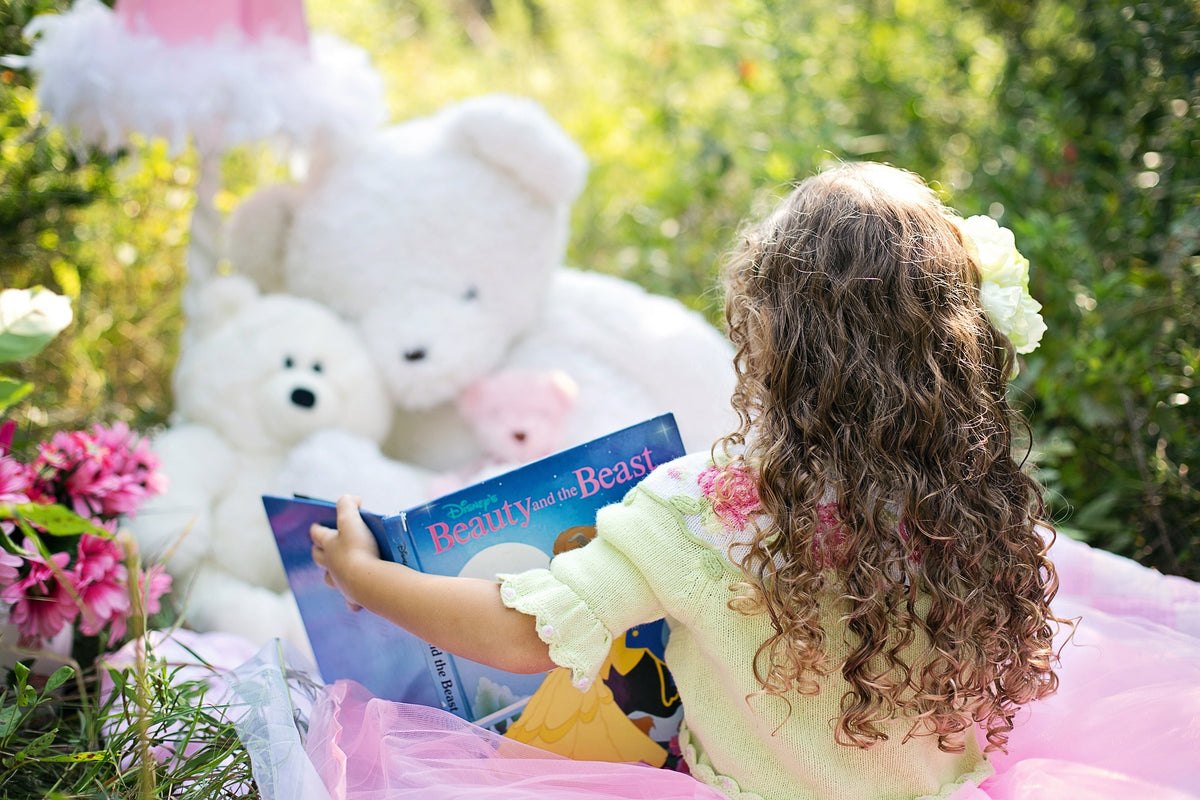 5-year-old girl has her back to the camera as she reads a book to her stuffed teddy bears on a blanket outside. At this age, your child may reach some early literacy milestones such as letter recognition and phonemic awareness.