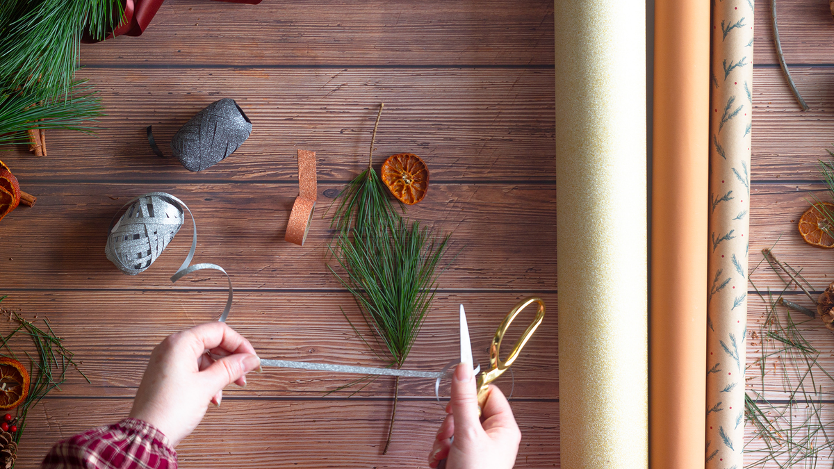 Multi-sensory Christmas themed art supplies lie scattered on a table while a pair of hands curl ribbon.