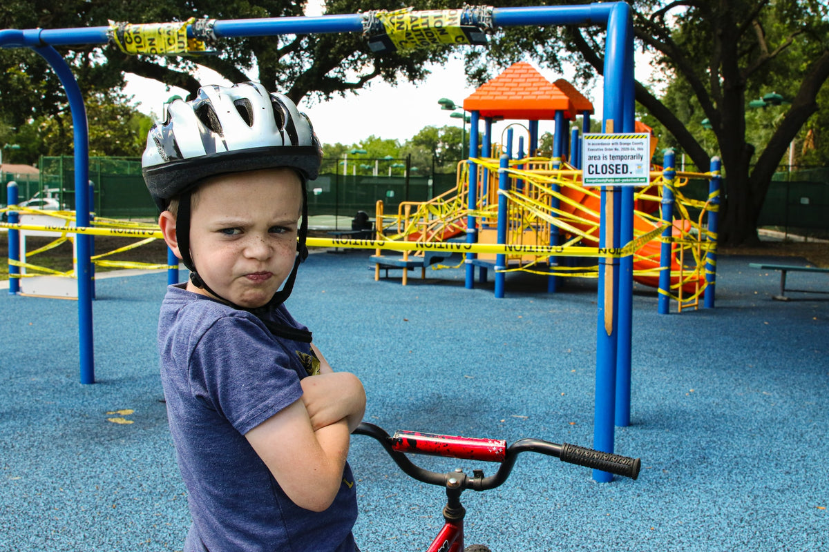 4-year-old boy on a bike at the playground crosses his arms and wears a displeased expression on his face. Identifying emotions is an important skill for a young child to have.