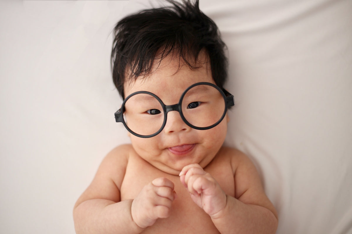 Baby lays on back wearing eyeglasses. He is developing important cognitive skills in his first year of life.