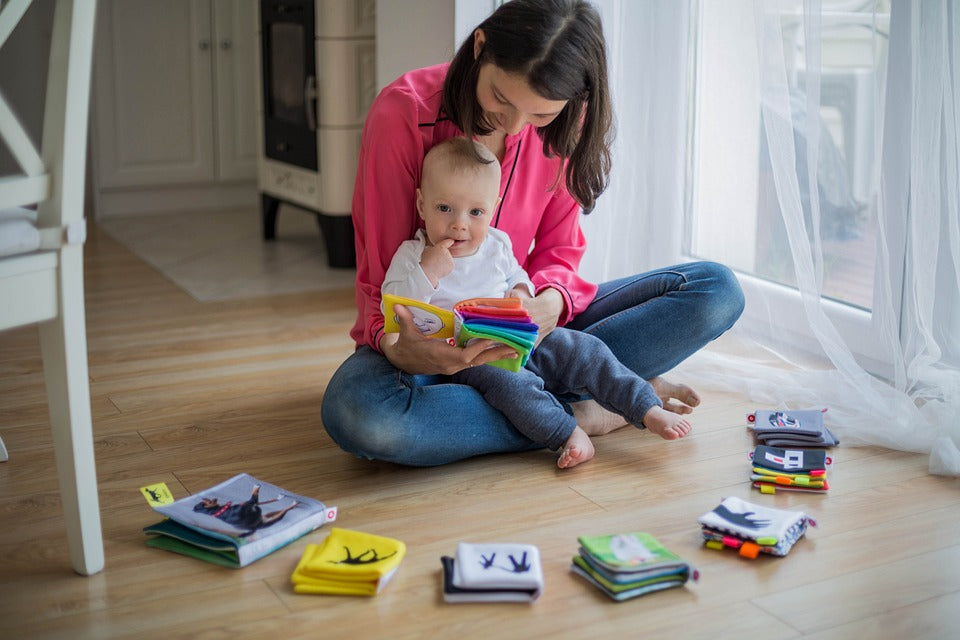 Mother sits her 1-year-old daughter in her lap and reads her a book. Even though your 1-year-old isn't able to read yet, reading to them interactively at this age is hugely beneficial to their future literacy.