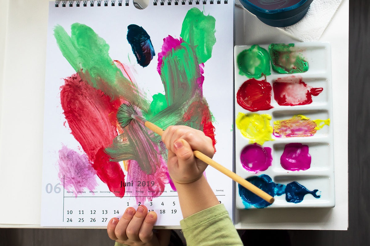 A pair of child's hands paint onto a calendar. In kindergarten, children will begin learning about calendar math in school, which will help them to solidify time concepts and engage with numbers.