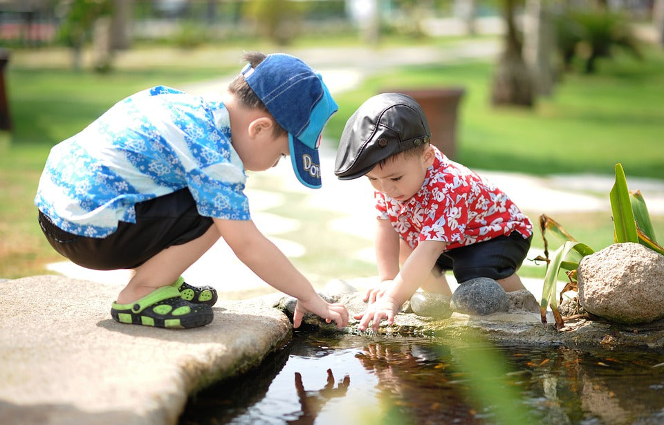 Two, small boys play together by manipulating items in a tiny pond. At 2-years-old, it is important to exercise your child's fine motor skills by allowing them to play with objects that exercise the muscles in their hands.