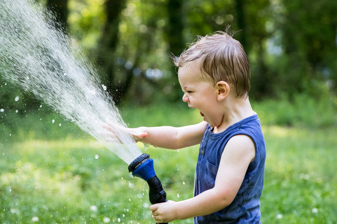 3-year-old boy laughs with glee as he plays with the water coming out of a garden hose. Letting your child take risks is one factor of raising independent children.
