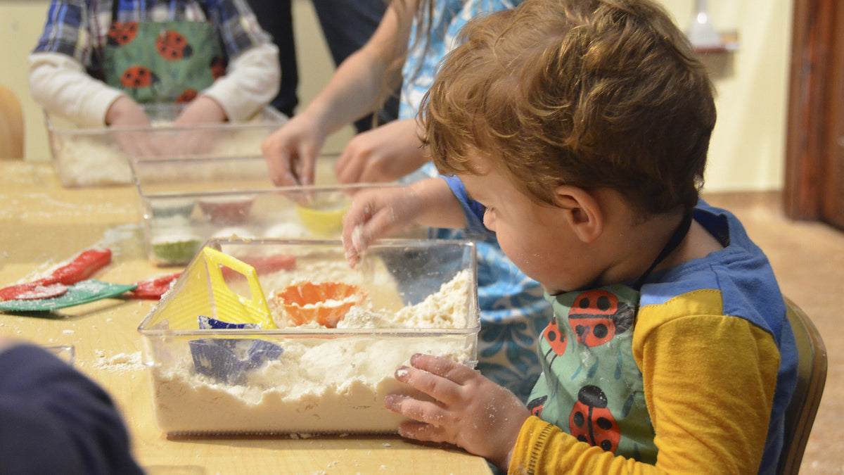 Three children engage in sensory play by exploring sand and toys in a sensory bin.