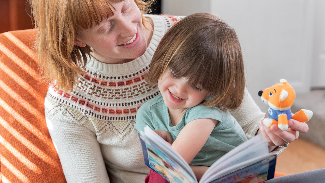 Toddler girl sits on mother's lap, reading, while mother holds book and Storypod's Craftie Fox