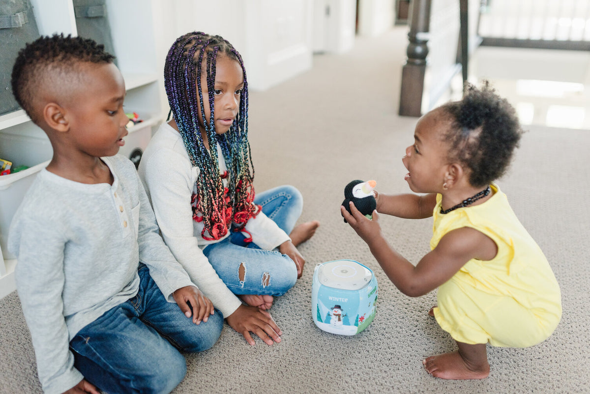 Two-year-old girl talks excitedly with her older siblings while playing with the Storypod Tali Tucan Craftie. Communicating verbally with family is one of the best ways to encourage language development in your 2-year-old.