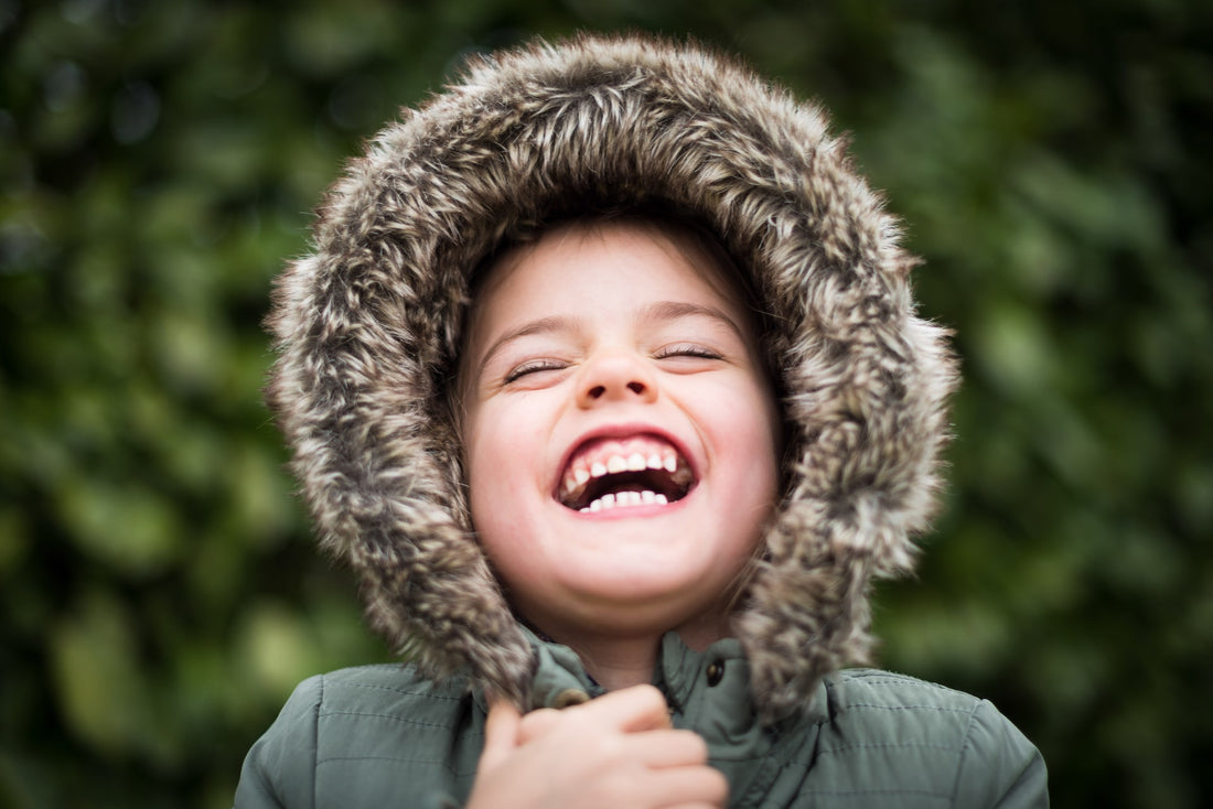 4 year old girl with a fur-trimmed hood closes eyes and laughs. There are many milestones to look forward to with your four-year-old, including an increase in social emotional skills.