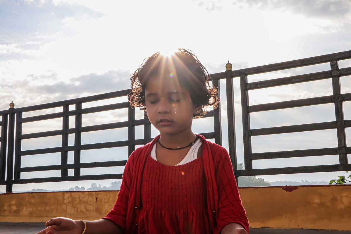 Preschool girl sits in yoga pose outside, eyes closed. Teaching children how to be mindful is important for their social emotional development.