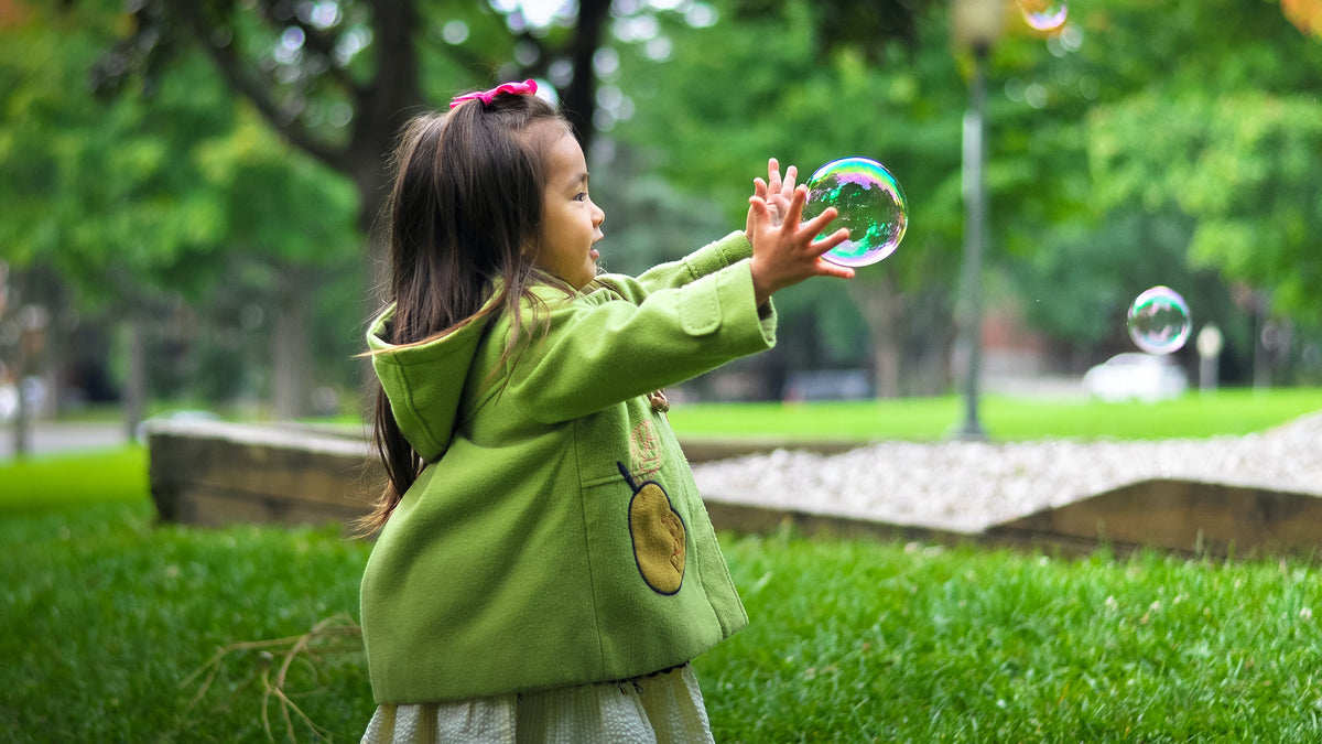 Happy little girl chases bubble outside