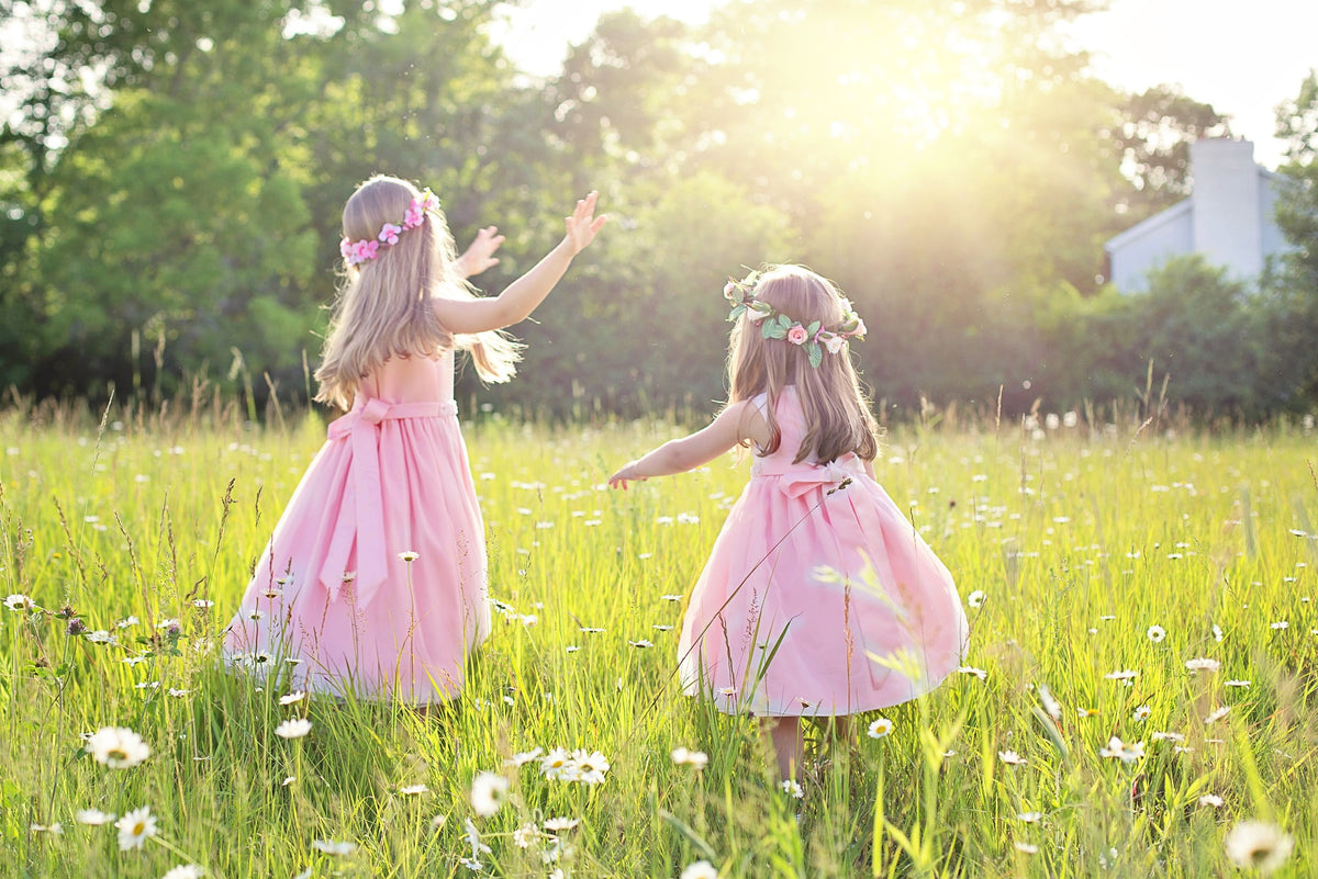 Two little girls wear pink dresses and flowers in their hair as they engage in narrative play in a field. Narrative play is an essential part of your 4-year-old's development as it helps them develop social skills, language skills, among other things.