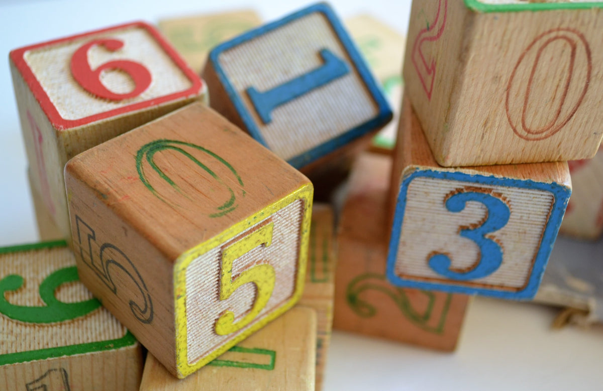 Children's wooden blocks with numbers on them lay scattered on a surface. Toddlers may begin counting and getting familiar with numbers as early as the age of 2.
